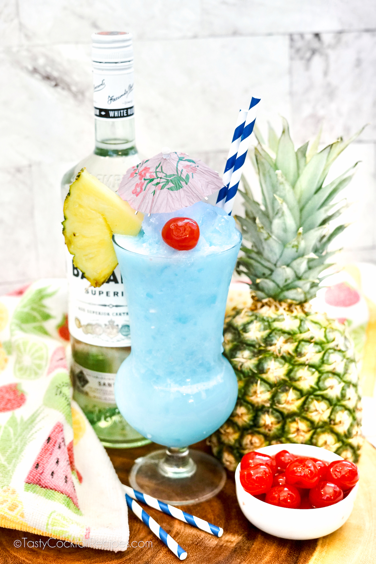 frozen Blue Hawaiian cocktail in hurricane glass, with a pineapple and bottle of rum