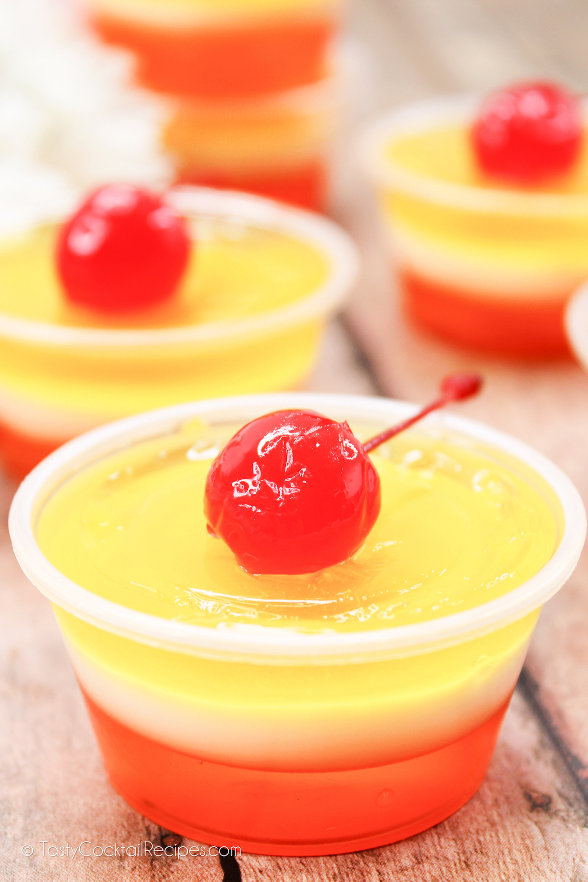 Piña Colada Jello Shots: yellow, white, and orange layers, with a cherry on top